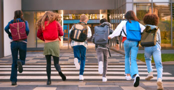 Gruop of 6 students running away from camera towards school