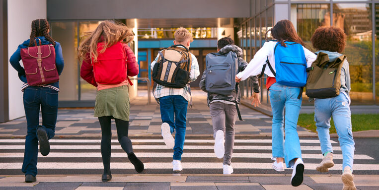Gruop of 6 students running away from camera towards school