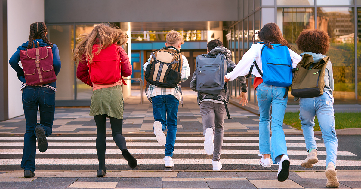 Gruop of 6 students running away from camera towards school